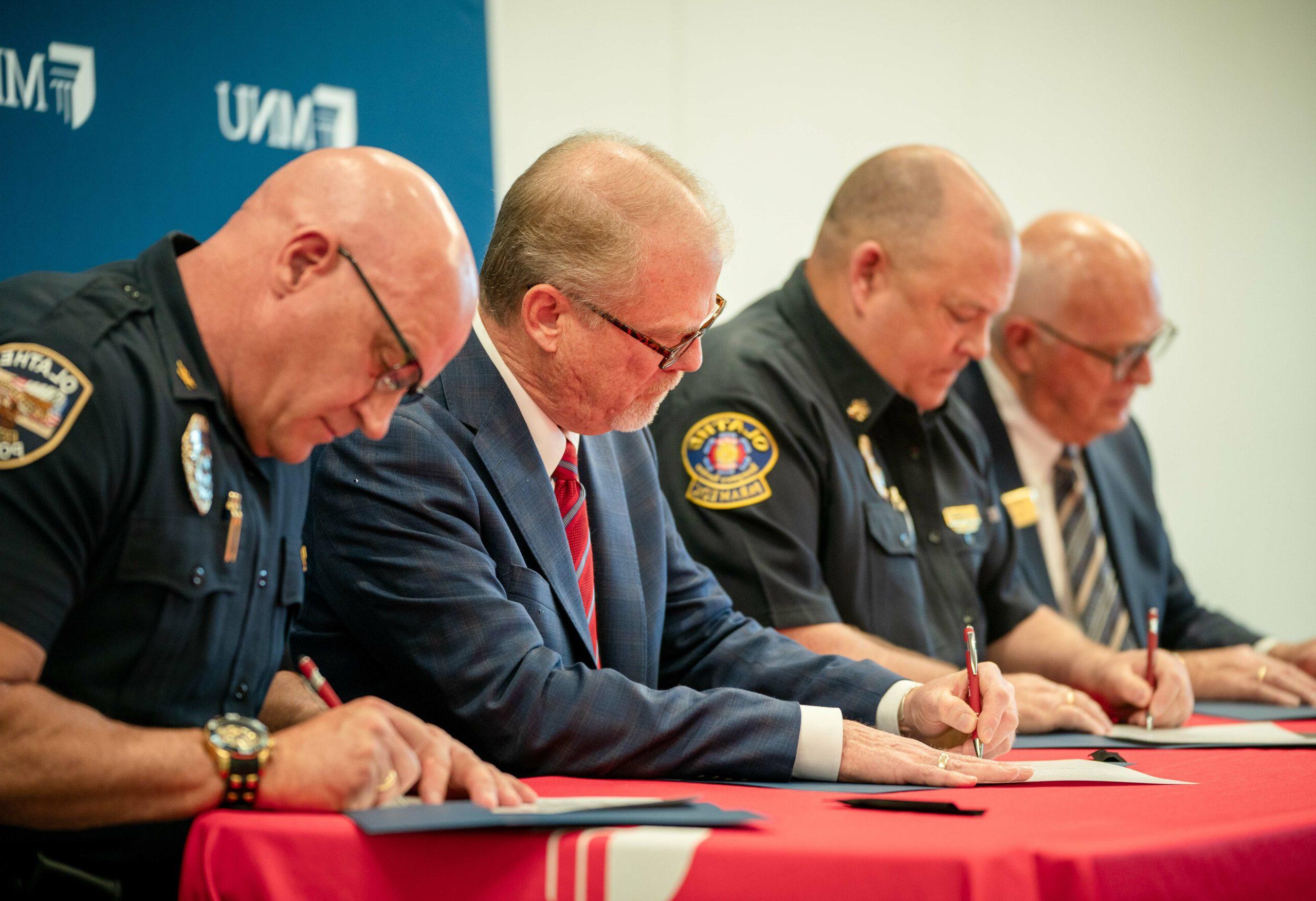 MNU主席大卫·斯皮塔尔说, 消防队长杰夫·德格拉夫里德说, Mayor John Bacon and Police Chief Mike Butaud signing 奖学金 agreement
